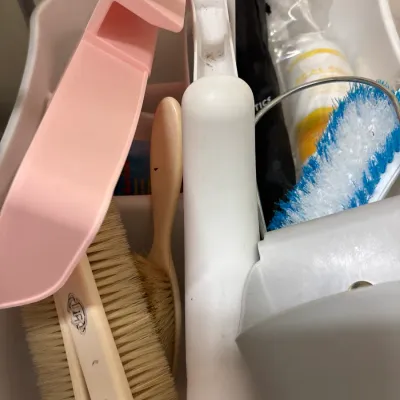 White plastic cleaning caddy filled with various household cleaning supplies, including a pink dustpan, scrub brushes, and spray bottles.