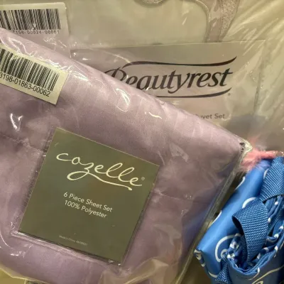 Packaged modern bedding items including a Cozelle lavender 6-piece sheet set and a Beautyrest duvet set in original plastic wrapping.