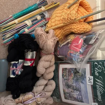 Assortment of knitting supplies, including various yarn skeins, single-pointed and double-pointed knitting needles, a partially completed...
