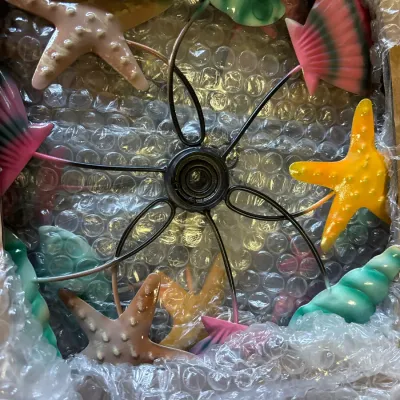 Ocean-themed metal kinetic wind spinner featuring colorful starfish and seashell blades, packed in its original shipping box.