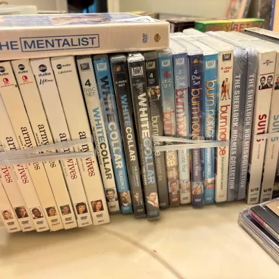 Large collection of TV show DVD box sets bundled with elastic bands, including titles like Army Wives, White Collar, Burn Notice, and Suits.