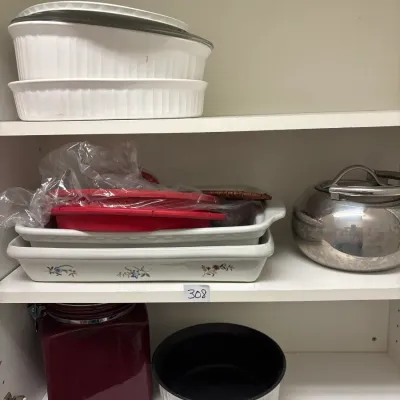 Assorted kitchenware including white CorningWare-style baking dishes, a stainless steel kettle, and a burgundy storage canister stacked...