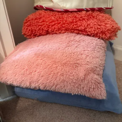 Stack of colorful throw pillows featuring shag plush texture in pink and coral along with a blue velvet floor cushion.