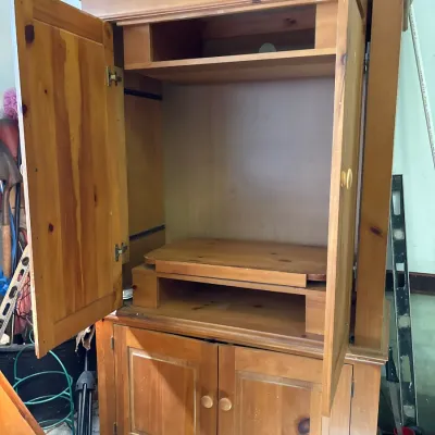 Large knotty pine entertainment armoire featuring carved crown detailing, upper television compartment with sliding doors, and lower...