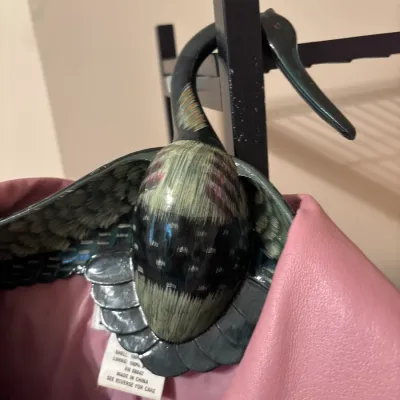 Novelty hand-painted wooden goose coat hanger supporting a pink leather jacket on a garment rack.
