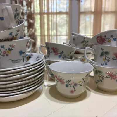 Vintage floral pattern porcelain teacup and saucer set, featuring stacked plates and matching cups with delicate botanical designs.