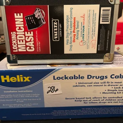 Vaultz locking medicine case with metal trim sitting on top of a Helix lockable drugs cabinet box.