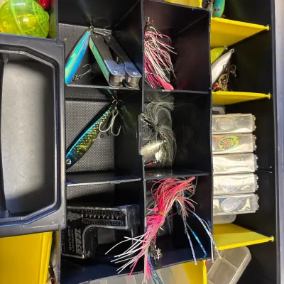 Yellow and black tackle organizer tray filled with various fishing accessories, including spoons, skirts, a multitool, and a vintage...