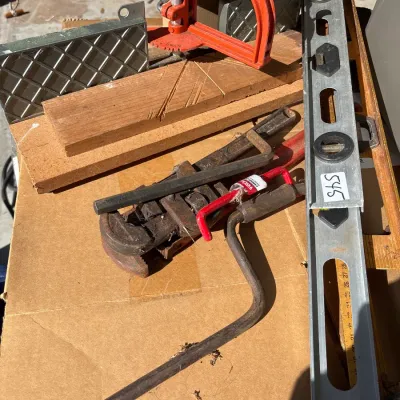 Assorted vintage hand tools, including an orange miter saw guide, heavy-duty pipe wrenches, a manual hand brace, and aluminum levels...