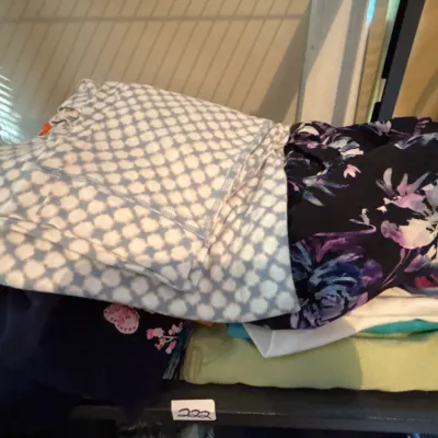 Folded pile of assorted women's clothing, including patterned leggings, tops, and casual wear.