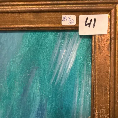 Close-up detail of a framed turquoise and blue painting featuring a carved gilt wood frame with sale lot tags.