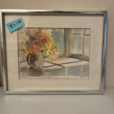 Framed watercolor painting depicting a bouquet of flowers in a pitcher on a window sill, set in a white mat and simple metallic silver...