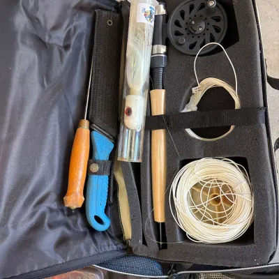Portable fly fishing kit in a zippered foam-padded soft case, including a rod handle, reel, line, lure, and fillet knife.