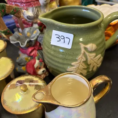 Collection of decorative ceramics featuring a green pitcher with raised leaf motifs and an iridescent cream and gold creamer and sugar set.