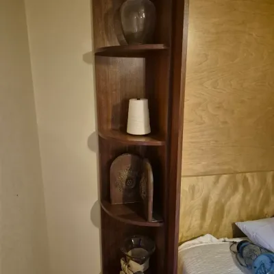 Sale Photo Thumbnail #69: Tall dark wood corner shelving unit displaying glass vases, a candle, and decorative bookends next to a bed.