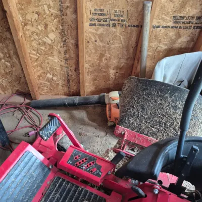 Sale Photo Thumbnail #115: Red zero-turn lawn mower and a gas-powered Stihl leaf blower stored in a shed.