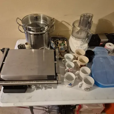 Sale Photo Thumbnail #63: Collection of small kitchen appliances including a Breville stainless steel contact grill and sandwich press, Cuisinart food processor, and large stockpot with steamer basket, displayed alongside assorted coffee mugs.
