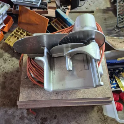 Sale Photo Thumbnail #97: Vintage electric meat slicer in aluminum finish with an orange extension cord wrapped around the base.