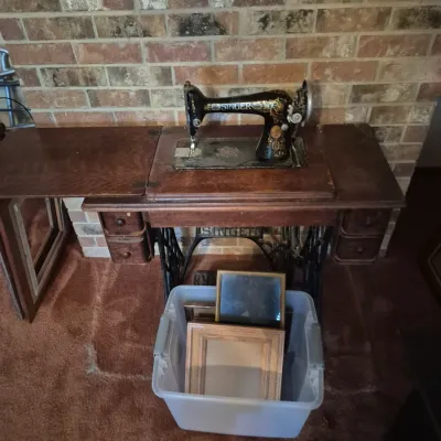 Sale Photo Thumbnail #40: Vintage Singer treadle sewing machine set in a dark wood cabinet with cast iron base, shown alongside a plastic bin filled with picture frames.