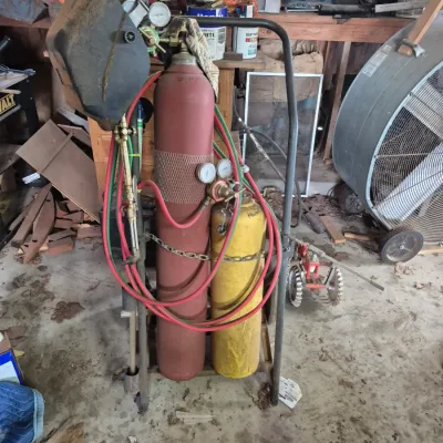 Sale Photo Thumbnail #103: Portable oxy-acetylene welding cart set with dual tanks, gauges, hoses, torch, and an attached welding mask.