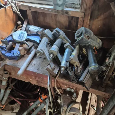 Sale Photo Thumbnail #87: Assortment of dusty pneumatic nail guns, bar clamps, and hand tools stored on a wooden workshop shelf.