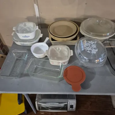Sale Photo Thumbnail #48: Collection of vintage bakeware, including CorningWare casserole dishes, clear glass baking pans, and stoneware pieces displayed on a table.