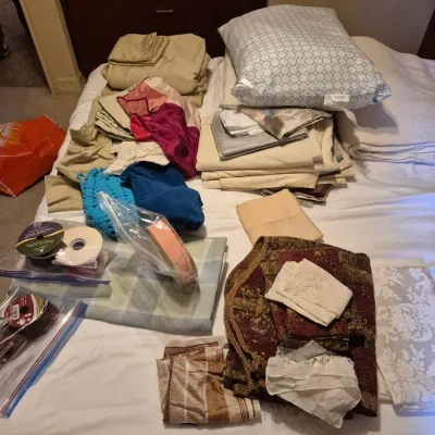 Sale Photo Thumbnail #61: Assortment of household linens, fabrics, pillows, and crafting ribbons laid out on a bed.