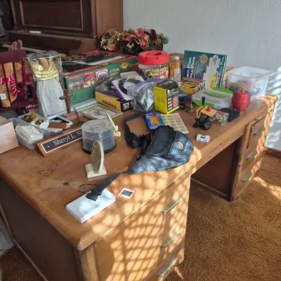 Sale Photo Thumbnail #18: Vintage mid-century wooden executive desk with multiple drawers, topped with various household knick-knacks, office supplies, and holiday decorations.