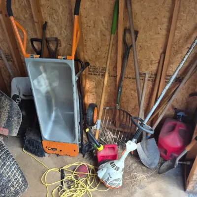 Sale Photo Thumbnail #107: Collection of yard work tools including a Worx Aerocart wheelbarrow, Stihl string trimmer, shovels, pitchfork, and gas cans.