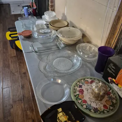 Sale Photo Thumbnail #43: Folding table displaying assorted vintage kitchenware, including Pyrex covered casseroles, clear glass baking dishes, serving trays, and decorative items.