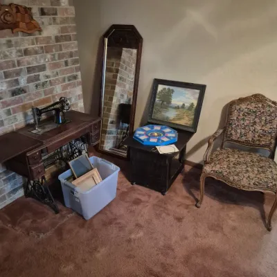 Sale Photo Thumbnail #31: Collection of vintage home furnishings including a treadle sewing machine table, tall wooden mirror, floral upholstered armchair, side table, framed landscape painting, and assorted picture frames in a tote.