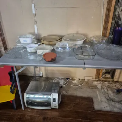 Sale Photo Thumbnail #3: Collection of vintage glassware and bakeware, including CorningWare, Pyrex, and clear casserole dishes on a folding table, with a toaster oven below.
