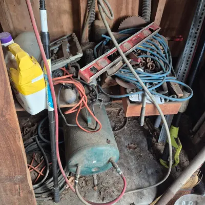 Sale Photo Thumbnail #88: Assorted workshop tools and equipment, including an old green air compressor tank, level, extension cords, and yard tools.