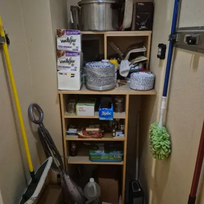 Sale Photo Thumbnail #59: Storage closet organized with wooden shelving units, stocked with household cleaning supplies, paper products, cookware, and floor mops.
