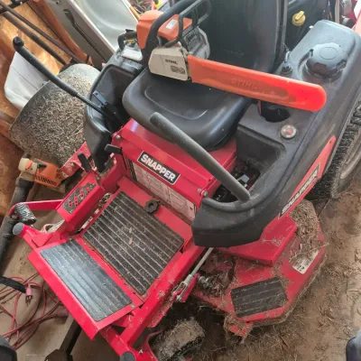 Sale Photo Thumbnail #113: Snapper red zero-turn riding lawn mower with a Stihl chainsaw sitting on the seat.