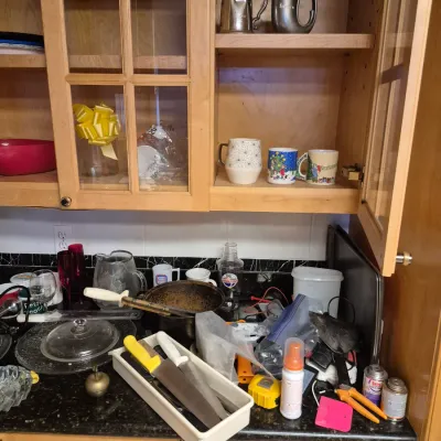 Sale Photo Thumbnail #58: Light wood kitchen cabinets containing pewter steins and coffee mugs above a countertop filled with various housewares and kitchen tools.