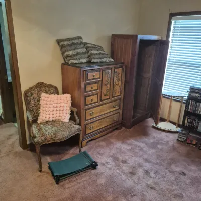 Sale Photo Thumbnail #30: Vintage bedroom setup featuring a French Provincial armless armchair with floral upholstery, a multi-drawer Asian-inspired wooden chest, and an open wooden wardrobe cabinet.