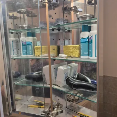 Sale Photo Thumbnail #80: Open mirrored medicine cabinet filled with personal care items, including electric razors, toiletries, and small bathroom accessories.