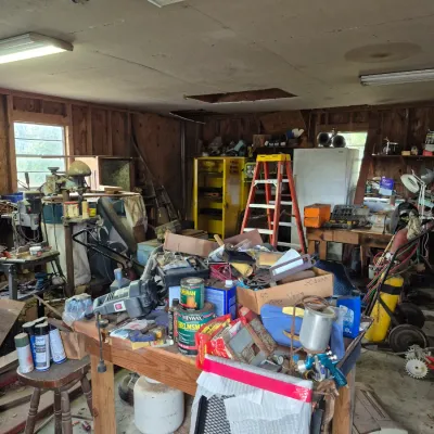 Sale Photo Thumbnail #89: Workshop and garage area filled with power tools, hand tools, painting supplies, a stepladder, and various equipment.