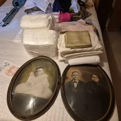 Sale Photo Thumbnail #67: Pair of antique oval convex glass framed portraits depicting a baby and a couple, shown alongside a collection of linens and craft supplies on a bed.