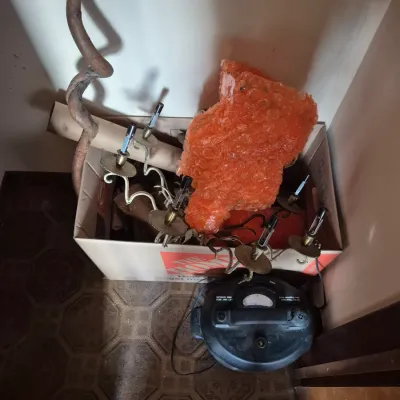 Sale Photo Thumbnail #84: Box containing an unscrewed light fixture, orange bubble-wrapped item, and a curved wooden staff alongside a small black shop vacuum.
