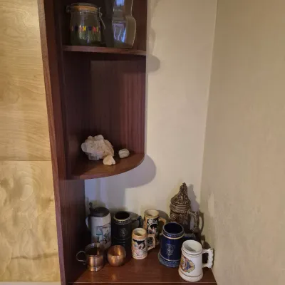 Sale Photo Thumbnail #60: Dark wood corner display cabinet with lower cabinet doors, featuring a collection of ceramic beer steins, glass vases, and rock specimens on display.