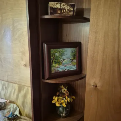 Sale Photo Thumbnail #68: Built-in wooden corner shelving unit featuring decorative display items, including a framed oil painting of a bridge over a stream and a vase with artificial flowers.