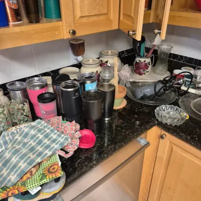 Sale Photo Thumbnail #57: Collection of kitchen items including insulated tumblers, travel mugs, immersion blender, glassware, ceramic canisters, and folded dish towels arranged on a countertop.
