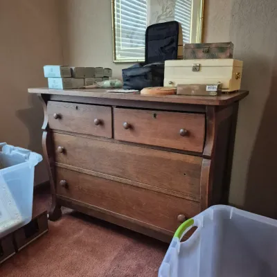 Sale Photo Thumbnail #33: Antique wooden Empire-style dresser featuring four drawers with wooden knobs and curved side posts, holding various boxes and small items on top.