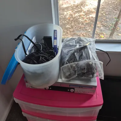 Sale Photo Thumbnail #75: Silver DVD player sitting atop a pink plastic three-drawer storage cart, holding a tub of assorted cables and packaged accessories.