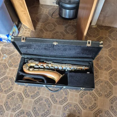 Sale Photo Thumbnail #81: Vintage brass saxophone showing finish wear and patina, resting in a black plush-lined hardshell carrying case.