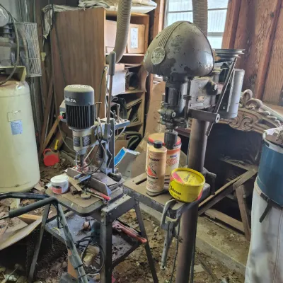 Sale Photo Thumbnail #96: Vintage Delta floor-standing drill press and a benchtop mortiser, shown with dust collection hoses and assorted workshop accessories in a garage setting.
