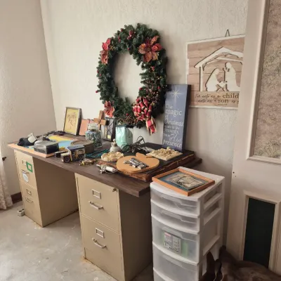 Sale Photo Thumbnail #16: Metal twin-pedestal desk topped with assorted holiday decor, framed wall art, and knick-knacks, alongside a plastic five-drawer storage cart.