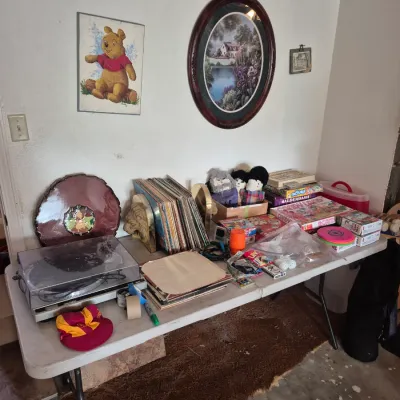 Sale Photo Thumbnail #38: Folding table displaying vintage vinyl records, a turntable, various board games, small collectibles, and wall art including a Winnie the Pooh print.